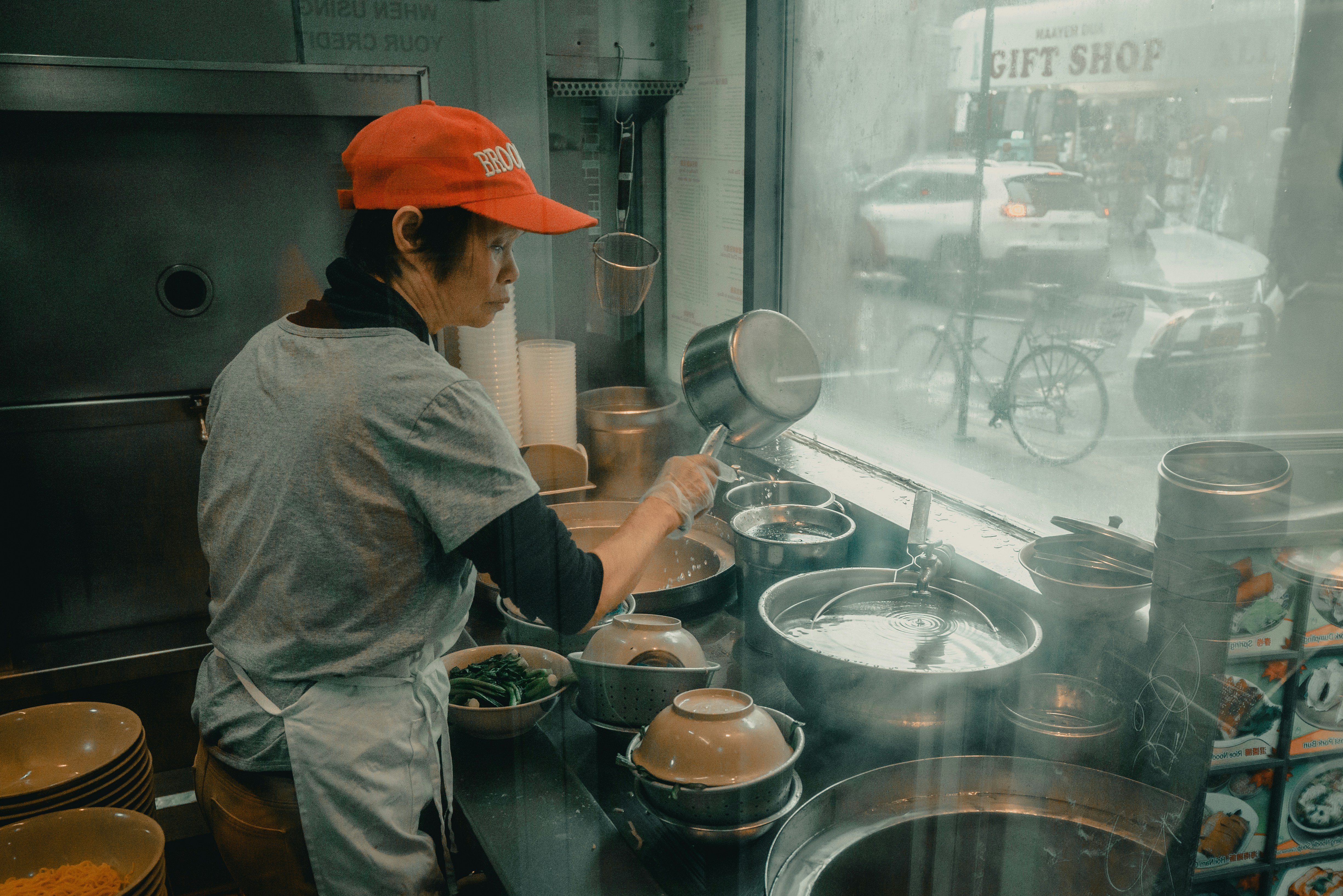 Cook preparing dishes at the kitchen window of a small Chinatown restaurant